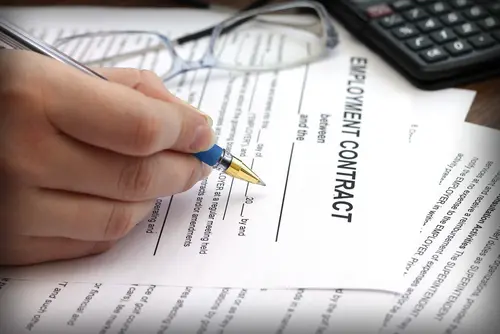 Signing employment contract with pen, calculator, and glasses - job offer paperwork.