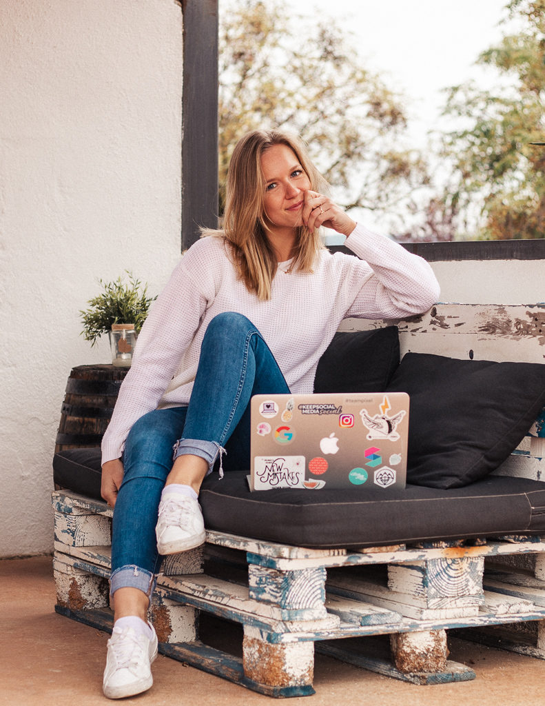 Remote worker on outdoor bench using laptop with creative tech stickers.
